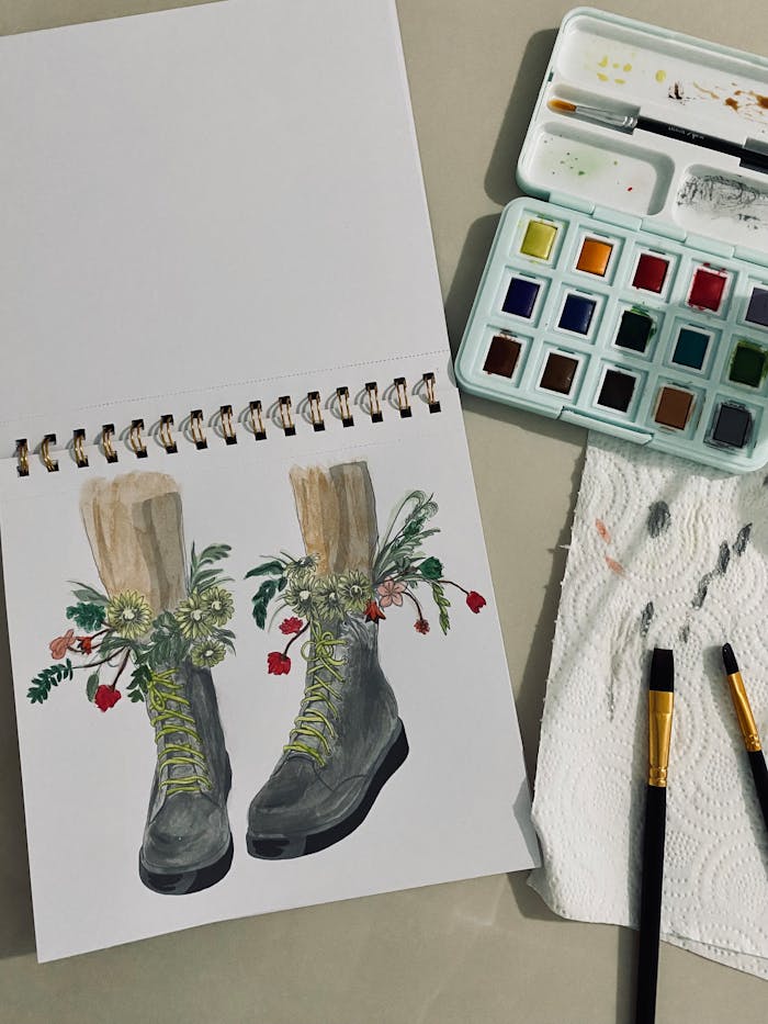 team-04 Watercolor painting of boots with floral design, accompanied by paints and brushes.